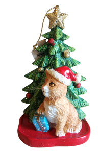 Brown Cat Sitting By Christmas Tree Wearing A Red Santa Hat Ornament