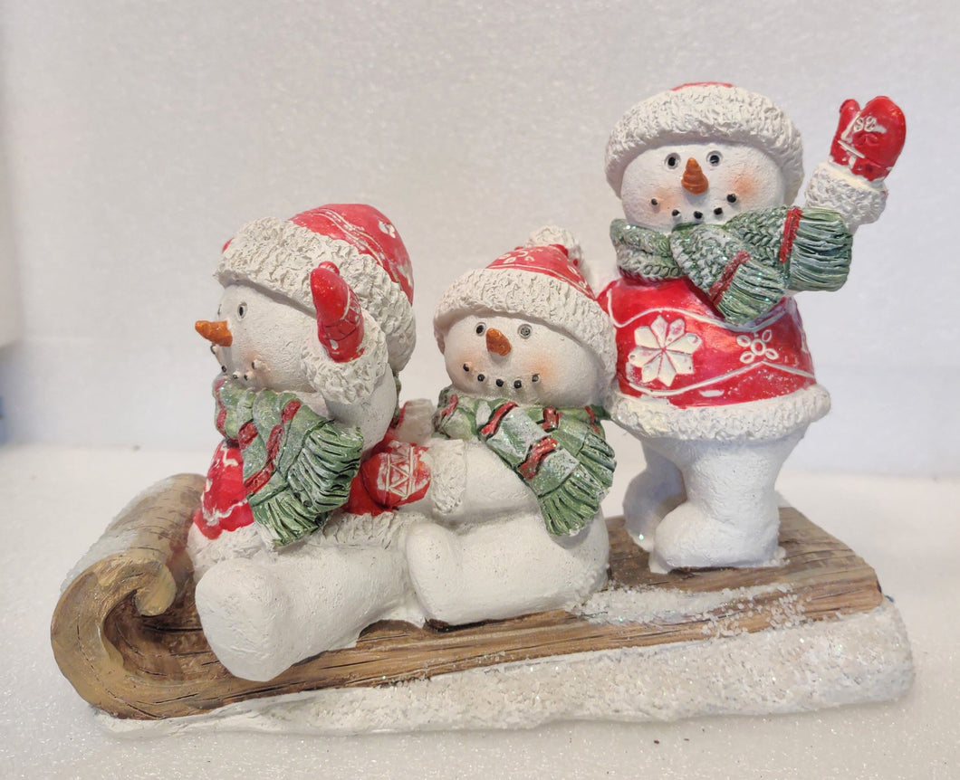 Three Snowman Sitting on Sled with Red Jackets/Red Hats & Green Scarves